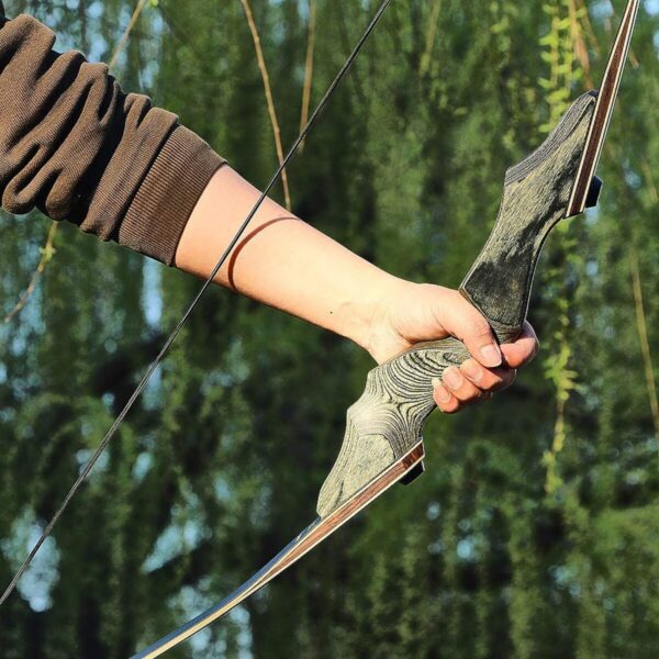 Person's hand holding a recurve bow, drawn and ready to shoot, with a blurred green background.